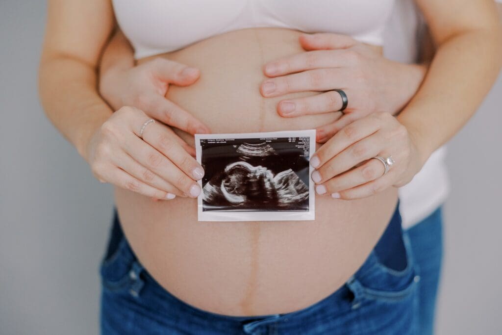 Mother and father pose with ultrasound photo during their maternity photo session