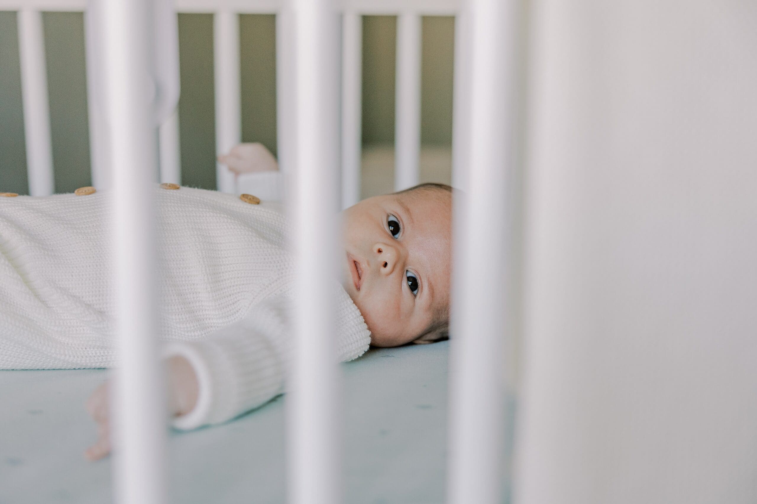 Baby laying in his crib during his lifestyle newborn photography session.