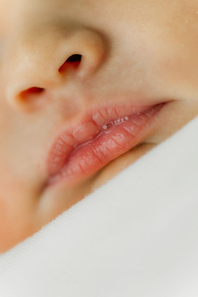 Baby Ember has lip bubbles during her in-home newborn photography session.