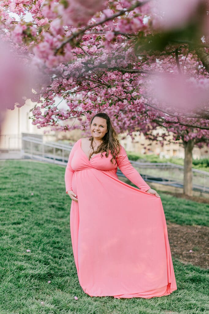 VMFA spring maternity photography featuring Shannon in a flowing pink dress with cherry blossoms and grand architecture.