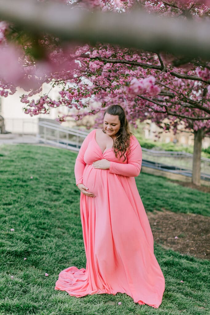 VMFA spring maternity photography featuring Shannon in a flowing pink dress with cherry blossoms and grand architecture.