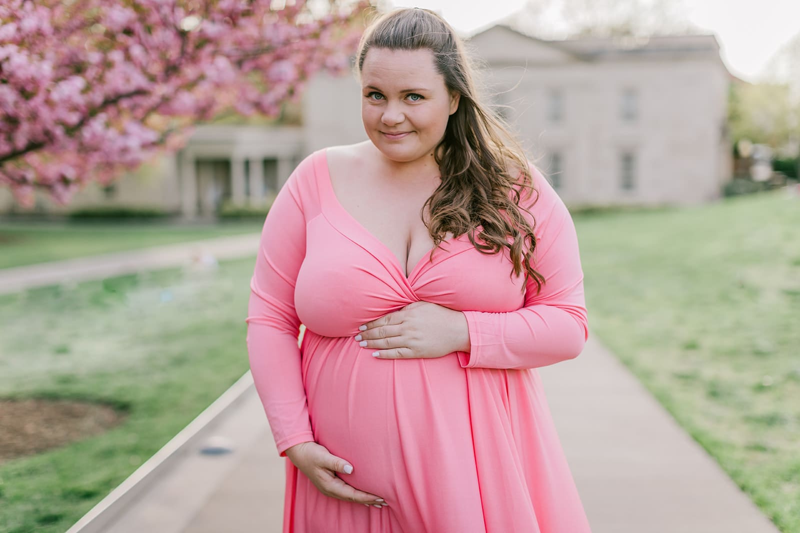 VMFA spring maternity photography featuring Shannon in a flowing pink dress with cherry blossoms and grand architecture.