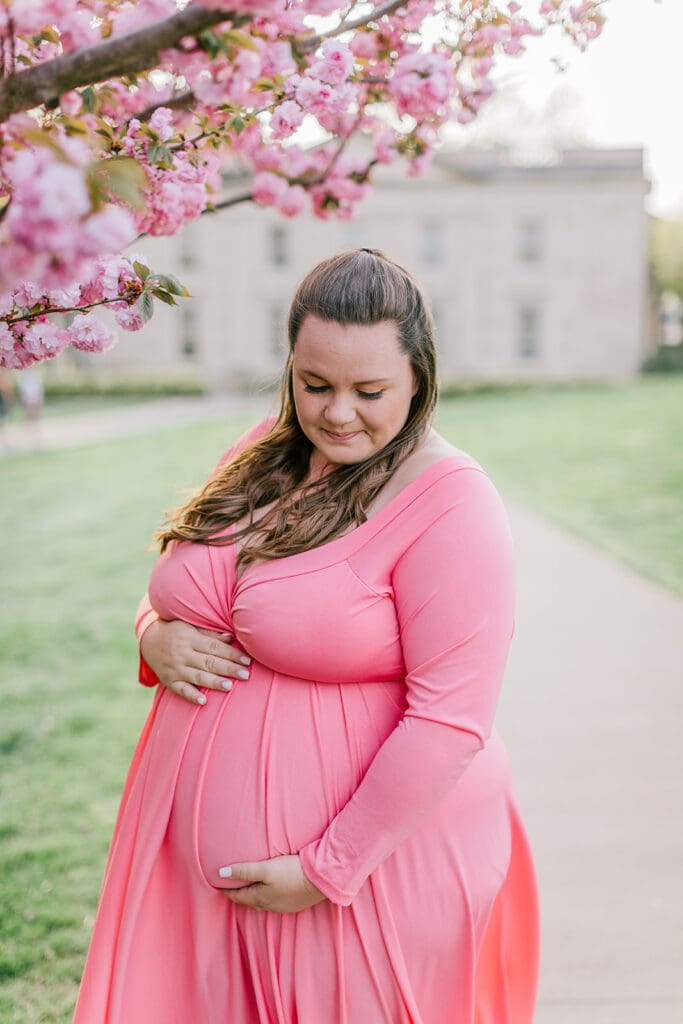 VMFA spring maternity photography featuring Shannon in a flowing pink dress with cherry blossoms and grand architecture.