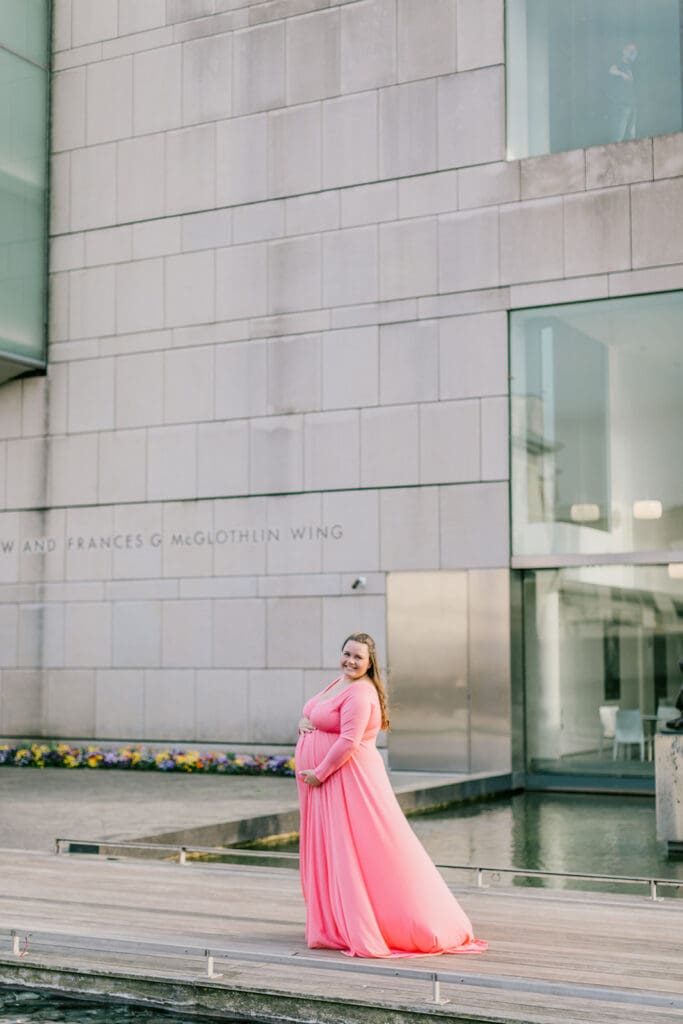 VMFA spring maternity photography featuring Shannon in a flowing pink dress with cherry blossoms and grand architecture.