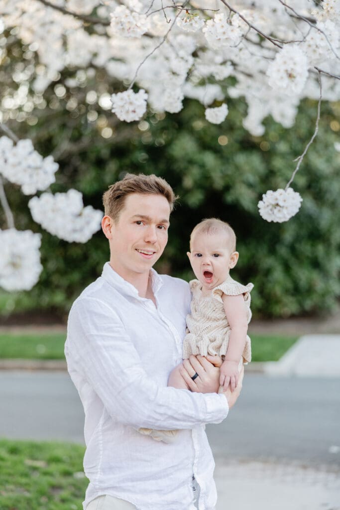 Family poses with their baby girl during their family photography session in the cherry blossoms in Richmond.