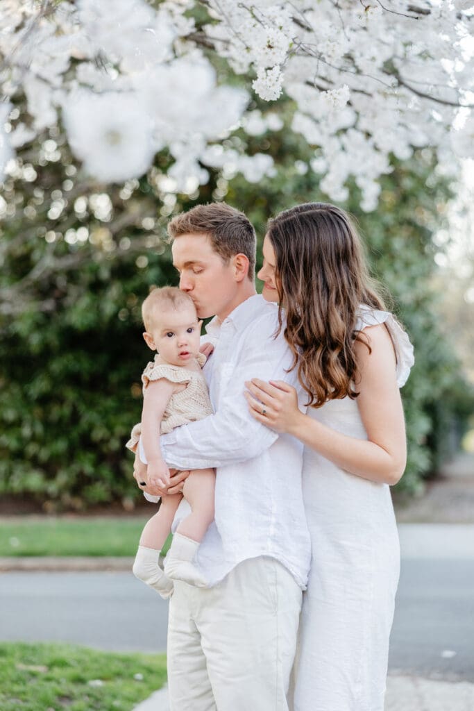 Family poses with their baby girl during their family photography session in the cherry blossoms in Richmond.