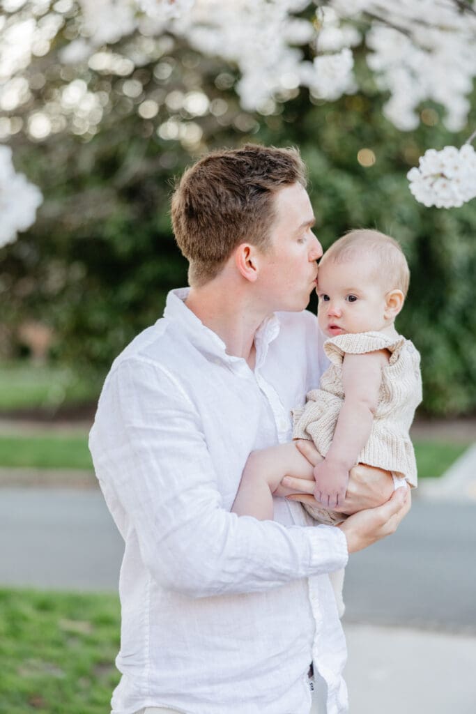 Family poses with their baby girl during their family photography session in the cherry blossoms in Richmond.